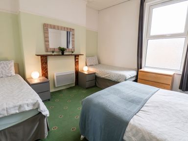 A bedroom with two single beds and one double bed a window a wooden chest of drawers and two bedside tables with lamps at Promenade in Bridlington