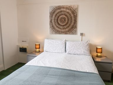A bedroom with a double bed white and blue bedding two bedside tables with lamps and circular wall art at Promenade in Bridlington
