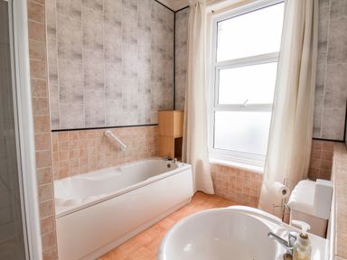 A bathroom with a bathtub sink toilet and a window with curtains at Promenade in Bridlington