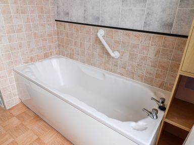 A bathroom with a white bathtub surrounded by tiled walls and wooden shelves at Promenade in Bridlington