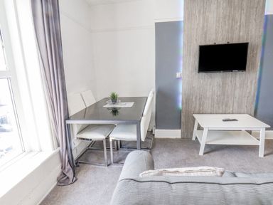 A dining area with a table and chairs next to a window and a wall-mounted TV above a coffee table at Ocean Wave in Bridlington