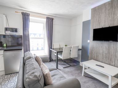 A living room with grey sofa, dining table with chairs, wall-mounted TV, and kitchen appliances at Ocean Wave in Bridlington