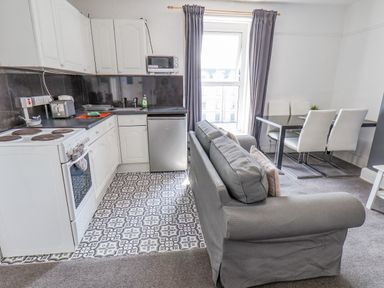 A kitchen and dining area with a gray sofa and patterned floor at Ocean Wave in Bridlington