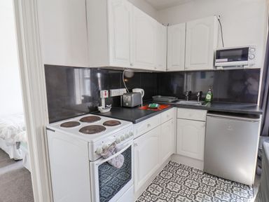 A kitchen with white cabinets a stove a toaster a microwave a sink and a small refrigerator at Ocean Wave in Bridlington