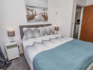 A bedroom with a double bed two bedside tables with lamps and a beach painting on the wall at Ocean Wave in Bridlington