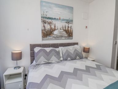 A bedroom with a bed with zigzag patterned bedding two bedside tables with lamps and a beach painting on the wall at Ocean Wave in Bridlington