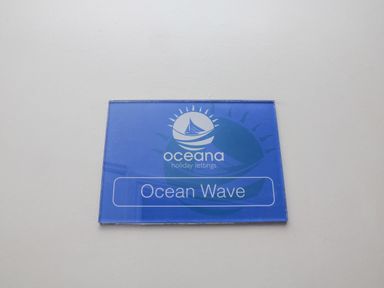 A blue sign with a white boat and sun logo reading Ocean Wave at Oceana holiday lettings