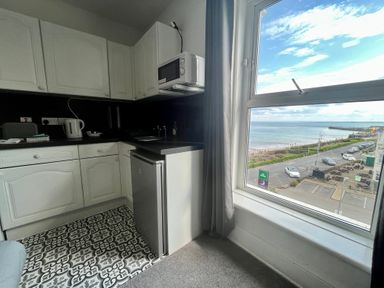 A small kitchen with white cabinets a mini fridge a microwave a kettle and a window overlooking a beach at Ocean Wave in Bridlington