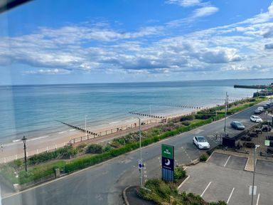 A coastal road with parked cars and a beach with wooden groynes at Ocean Wave in Bridlington