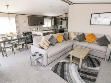 An open living room and kitchen with a corner sofa with cushions a coffee table and a dining table with chairs at Beechwood Lodge in Hasguard Cross near Broad Haven