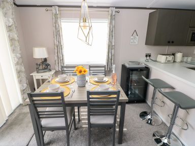 A dining area with a set table and four chairs next to a kitchen counter with two bar stools at Beechwood Lodge Hasguard Cross near Broad Haven