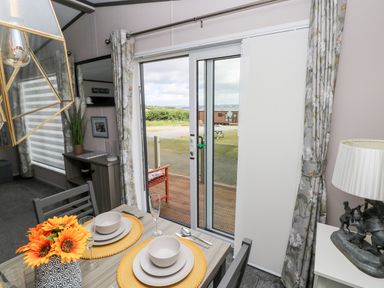 A dining area with a table set for two near sliding glass doors and a window with floral curtains at Beechwood Lodge in Hasguard Cross near Broad Haven