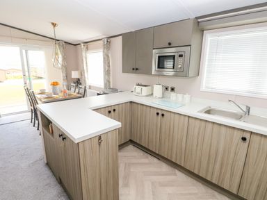 A kitchen with wooden cabinets a microwave kettle and toaster next to a dining area with a table and chairs at Beechwood Lodge in Hasguard Cross near Broad Haven