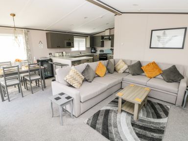 A living room with a grey sectional sofa and a wooden coffee table next to an open kitchen and dining area at Beechwood Lodge in Hasguard Cross near Broad Haven