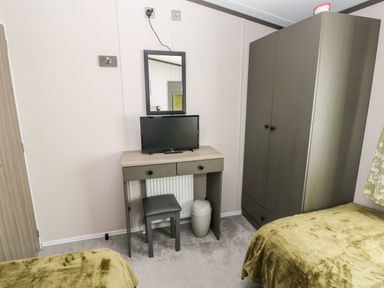 A bedroom with two beds a wardrobe a desk with a mirror a stool a television and a trash bin at Beechwood Lodge in Hasguard Cross near Broad Haven
