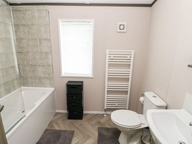 A bathroom with a bathtub shower combination a toilet a sink a window with blinds a black storage unit and a white heated towel rail at Beechwood Lodge in Hasguard Cross near Broad Haven