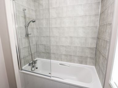 A bathroom with a bathtub shower combination and gray tiled walls at Beechwood Lodge Hasguard Cross near Broad Haven