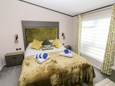 A bedroom with a double bed with pillows and towels beside a window with curtains at Beechwood Lodge Hasguard Cross near Broad Haven