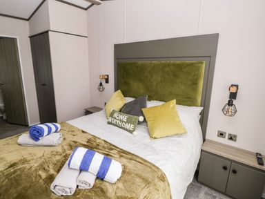 A bedroom with a double bed with pillows and towels a bedside table and a wardrobe at Beechwood Lodge in Hasguard Cross near Broad Haven