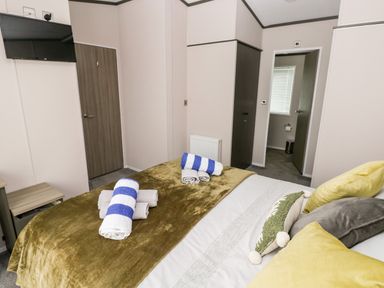 A bedroom with a bed with pillows and towels and a wall mounted television at Beechwood Lodge in Hasguard Cross near Broad Haven