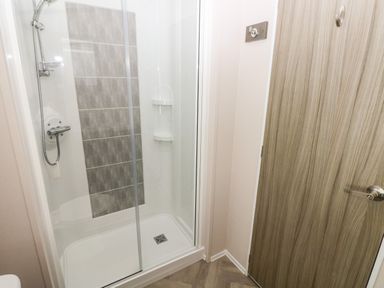 A shower enclosure with a glass door next to a wooden door in a bathroom at Beechwood Lodge Hasguard Cross near Broad Haven