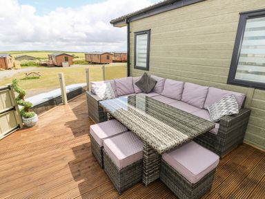 An outdoor seating area with a glass table and cushioned wicker chairs on a wooden deck at Beechwood Lodge in Hasguard Cross near Broad Haven