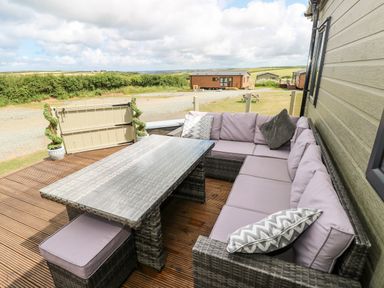 An outdoor patio with wicker sectional sofa and glass table at Beechwood Lodge in Hasguard Cross near Broad Haven