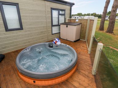 An outdoor hot tub on a wooden deck next to a building with two windows and a storage shed at Beechwood Lodge in Hasguard Cross near Broad Haven