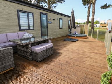 A wooden deck with wicker outdoor furniture and a hot tub outside a lodge at Beechwood Lodge in Hasguard Cross near Broad Haven