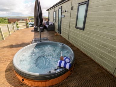 An outdoor deck with a hot tub towels umbrella and seating at Beechwood Lodge in Hasguard Cross near Broad Haven
