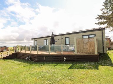 A mobile home with a wooden deck and glass railing on a grassy lawn at Beechwood Lodge Hasguard Cross near Broad Haven