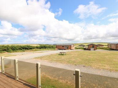 A row of wooden lodges and a picnic table in a grassy area with a glass balcony in the foreground at Beechwood Lodge Hasguard Cross near Broad Haven