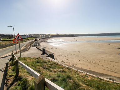 A coastal road next to a sandy beach with houses in the background at Beechwood Lodge in Hasguard Cross near Broad Haven