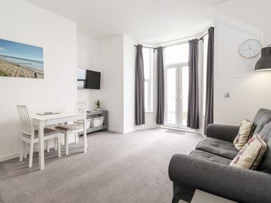 A living room with a gray sofa and coffee table near bay windows with gray curtains and a small dining table with two chairs at 3 Seaview @ Bridlington Bay in Bridlington