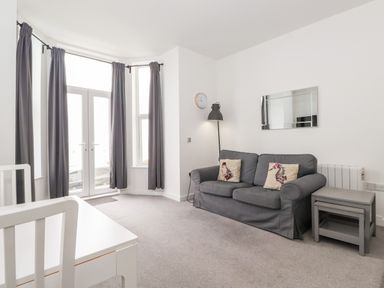 A living room with a gray sofa, floor lamp, wall clock, side tables, white dining table and chairs near windows with gray curtains at 3 Seaview @ Bridlington Bay in Bridlington