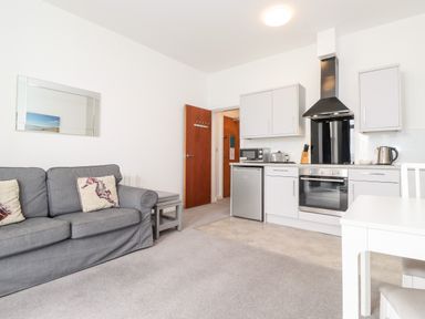 A living room with a grey sofa and pillows near a kitchen with white cabinets a fridge and an oven at 3 Seaview @ Bridlington Bay in Bridlington