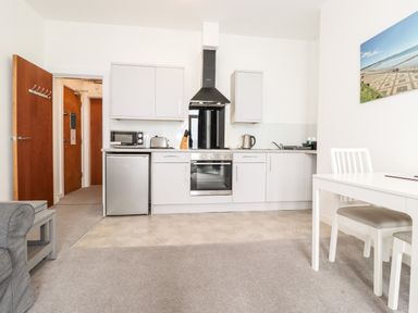 A kitchen area with white cabinets a microwave toaster and kettle a white dining table and chair at 3 Seaview @ Bridlington Bay in Bridlington
