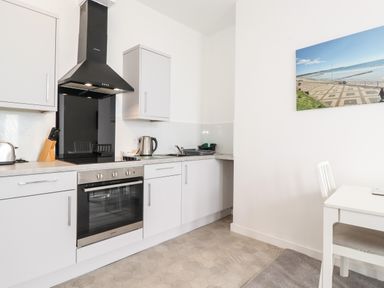 A kitchen with white cabinets a stainless steel oven a black range hood and a white table with a chair at 3 Seaview @ Bridlington Bay in Bridlington