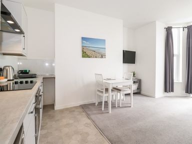 A kitchen area with appliances next to a small dining table and chairs in a room with windows and curtains at 3 Seaview @ Bridlington Bay in Bridlington