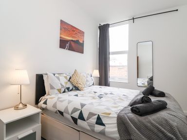 A bedroom with a bed covered in geometric patterned bedding two bedside lamps a tall window with curtains and a wall mirror at 3 Seaview @ Bridlington Bay in Bridlington