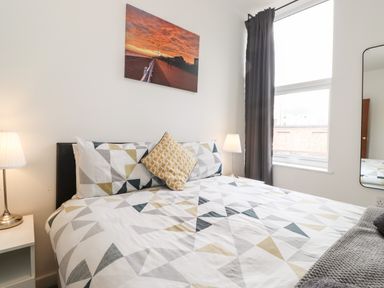 A bedroom with a bed with geometric patterned bedding two bedside lamps a window with dark curtains and a wall picture at 3 Seaview Bridlington Bay in Bridlington