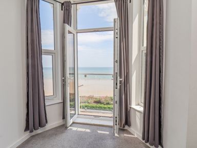 A room with open balcony doors overlooking a beach and sea at 4 Seaview @ Bridlington Bay in Bridlington