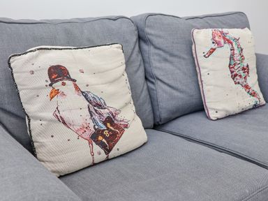 A gray sofa with two decorative cushions one with a bird in a hat and the other with a seahorse at 4 Seaview @ Bridlington Bay in Bridlington