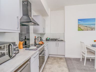 A kitchen with white cabinets a black stove a stainless steel oven a microwave and a dining table with chairs at 4 Seaview @ Bridlington Bay in Bridlington