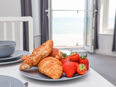 A plate with croissants and strawberries on a table next to stacked grey plates in a room with an open door showing a sea view at 4 Seaview @ Bridlington Bay in Bridlington