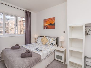 A bedroom with a double bed bedside tables lamps a shelving unit and a window with curtains at 4 Seaview Bridlington Bay in Bridlington