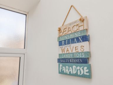 A hanging wooden sign with beach and sea-related words next to a frosted window at 4 Seaview @ Bridlington Bay in Bridlington