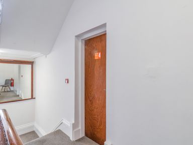 An indoor stairway landing with a wooden door labeled number 4 a mirror on the wall a gray chair and a fire extinguisher reflected in the mirror at 4 Seaview Bridlington Bay in Bridlington