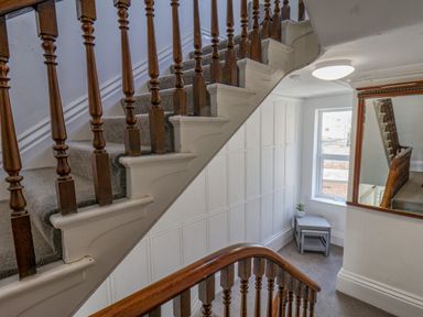 A staircase with wooden banisters and carpeted steps next to a window with a small table and plant at 4 Seaview @ Bridlington Bay in Bridlington