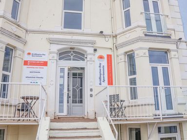 The entrance to Bridlington Bay Apartments with stairs leading to a glass door and small balconies with tables and chairs at 4 Seaview @ Bridlington Bay in Bridlington